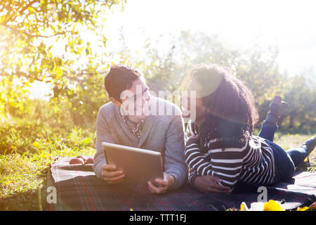 Cheerful couple using tablet computer while relaxing on blanket in orchard Stock Photo