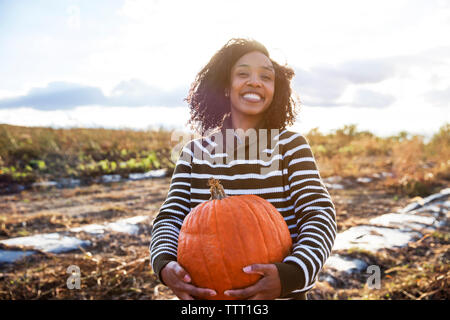 Portrait of woman carrying pumpkin while standing in farm against sky Stock Photo