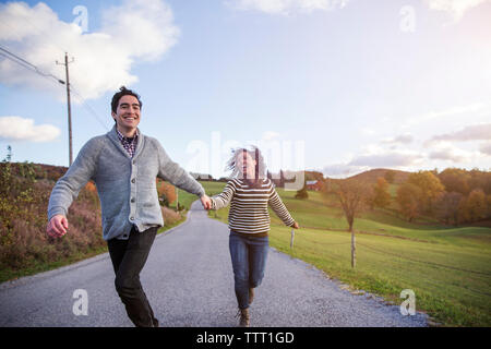 Cheerful couple running on footpath against sky Stock Photo