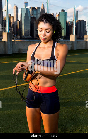 Female athlete using smart watch while standing on grassy field during sunset Stock Photo