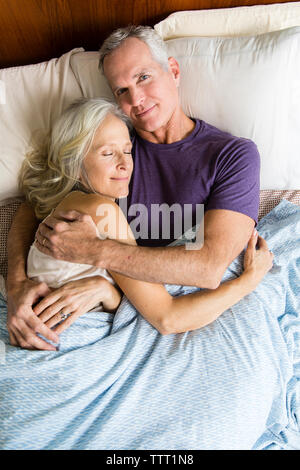 Overhead portrait of confident man lying with sleeping woman on bed at home Stock Photo