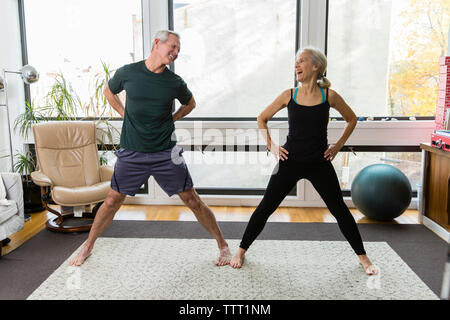 Cheerful couple exercising together against windows at home Stock Photo