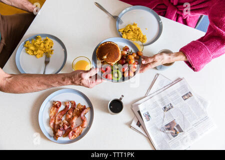 Midsection of couple holding plate with food over dining table at home