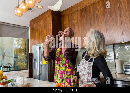 Cheerful man tossing pizza dough while preparing food by woman in kitchen Stock Photo