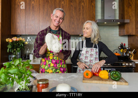 Woman cutting bell peppers while man making pizza dough in kitchen at home Stock Photo