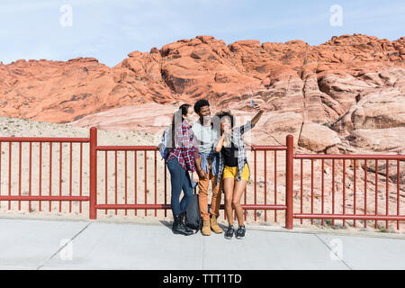 Friends talking selfie while standing by railing against sky at desert during sunny day Stock Photo
