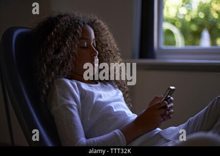 Girl using mobile phone while sitting on chair at home Stock Photo