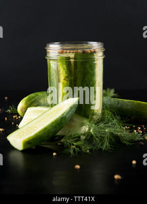 Close-up of pickles in jar by cucumbers on table Stock Photo