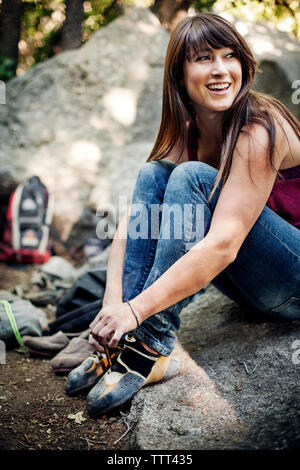 Smiling woman tying shoelace while sitting on rock Stock Photo