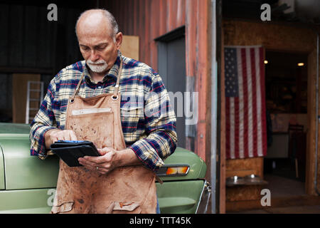 Senior craftsperson using digital tablet while standing outside workshop Stock Photo
