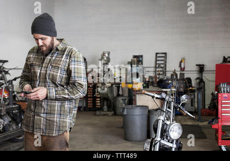 Smiling worker using phone while standing at auto repair shop Stock Photo