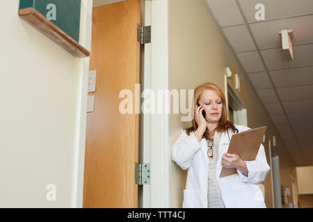 Female doctor talking on mobile phone while leaning on wall at hospital Stock Photo