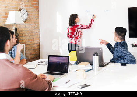 Colleagues looking at businesswoman writing on whiteboard during meeting in boardroom Stock Photo