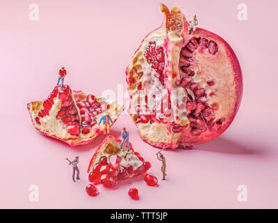 Close-up of miniature figurine workers crushing pomegranate on pink background Stock Photo
