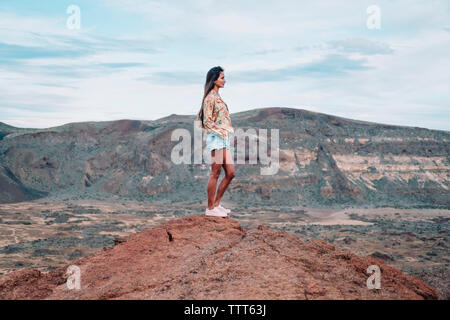 A woman stands on a rock formation against a mountain backdrop Stock Photo