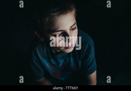 High angle view of thoughtful boy sitting in dark room Stock Photo