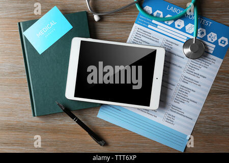 Stethoscope, tablet and laboratory test list on wooden table Stock Photo