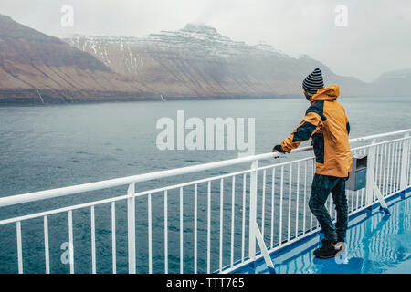 Side view of man standing by railing on boat during rainy season Stock Photo