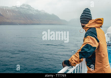 Side view of man looking at view while standing by railing on boat during rainy season Stock Photo
