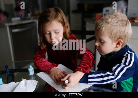 Sister painting brother's fingernails while sitting at table Stock Photo