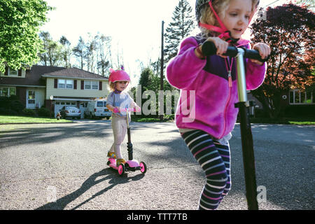 Sisters riding push scooters on road Stock Photo