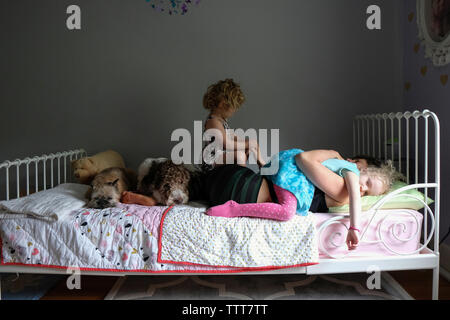 Daughters on mother with dogs lying on bed against wall at home Stock Photo