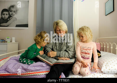 Grandmother telling story to granddaughters while sitting on bed at home Stock Photo