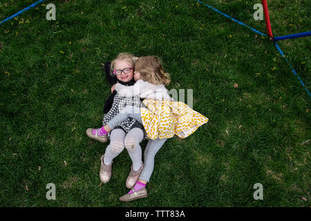 High angle view of happy sisters lying on grassy field at yard Stock Photo