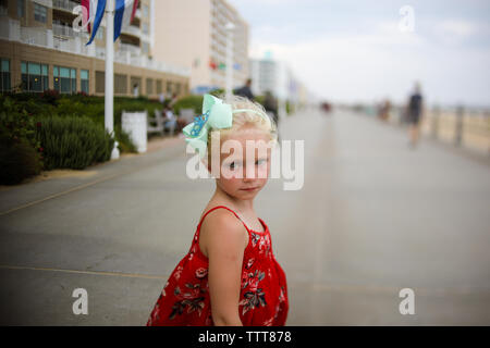 little girl in red dress on boardwalk big bow serious expression Stock Photo