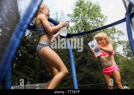 sisters laughing having water fight on trampoline in summer Stock Photo