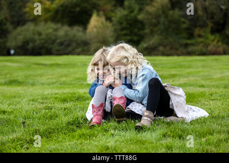 two sisters sitting on grass laughing and hugging together Stock Photo