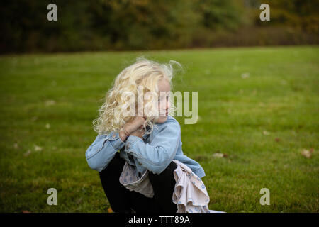 young girl crouching looking off into the distance in a field Stock Photo