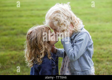 sisters giving each other kiss standing in field Stock Photo