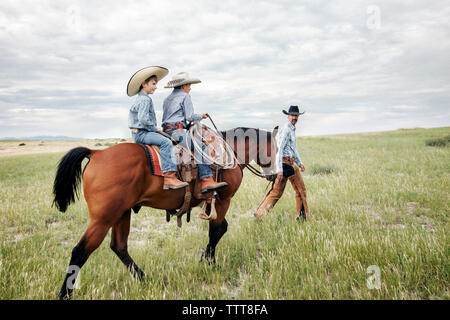 Father looking at sons riding horse on field against cloudy sky Stock Photo