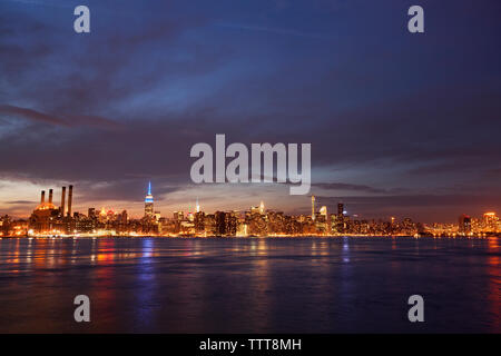 Scenic view of river and illuminated cityscape against cloudy sky at night