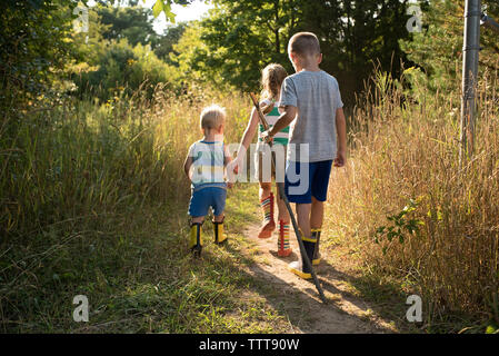 Rear view of siblings walking on field at forest Stock Photo