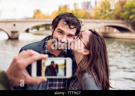 Cropped image of friend photographing couple through smart phone by river Stock Photo