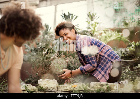 Happy woman looking at friend while gardening in community garden Stock Photo
