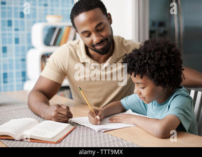 Father helping son with homework at table in home Stock Photo