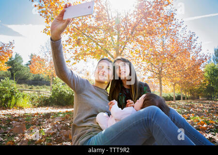 Smiling mother taking selfie with daughters at park during autumn Stock Photo