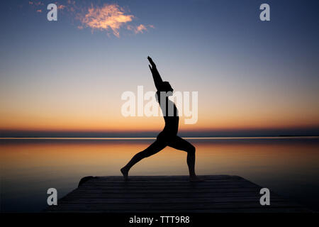 Silhouette woman exercising on pier against sky during sunset Stock Photo