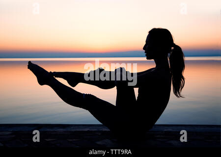 Side view of woman exercising against sea during sunset Stock Photo