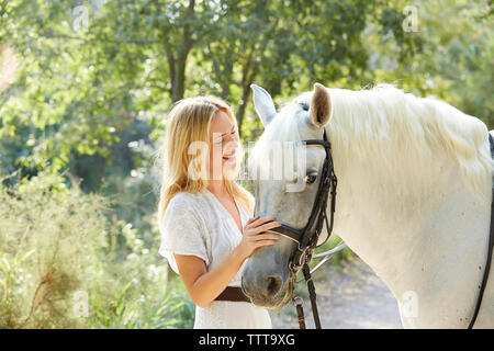 Happy woman stroking white horse in farm Stock Photo