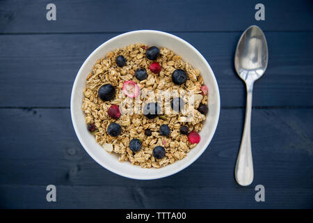 Overhead view of breakfast cereals served in bowl with spoon on wooden table Stock Photo