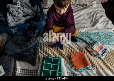 High angle view of boy folding clothes while sitting on bed at home Stock Photo