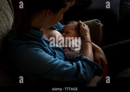 High angle view of mother breastfeeding newborn daughter while sitting on sofa at home Stock Photo