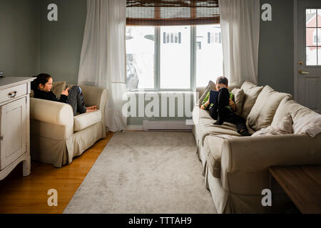Siblings using wireless technology while relaxing in living room at home Stock Photo