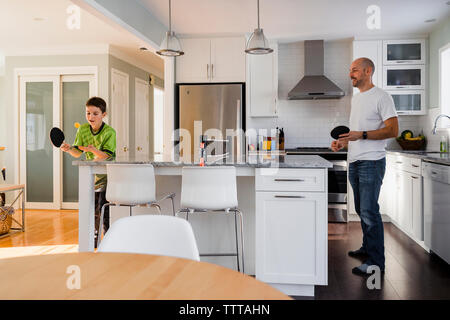 Son playing table tennis with father on kitchen island at home Stock Photo