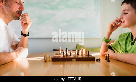 Son playing chess with father on table at home Stock Photo