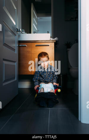 Portrait of boy defecating while sitting on potty seen through doorway at home Stock Photo